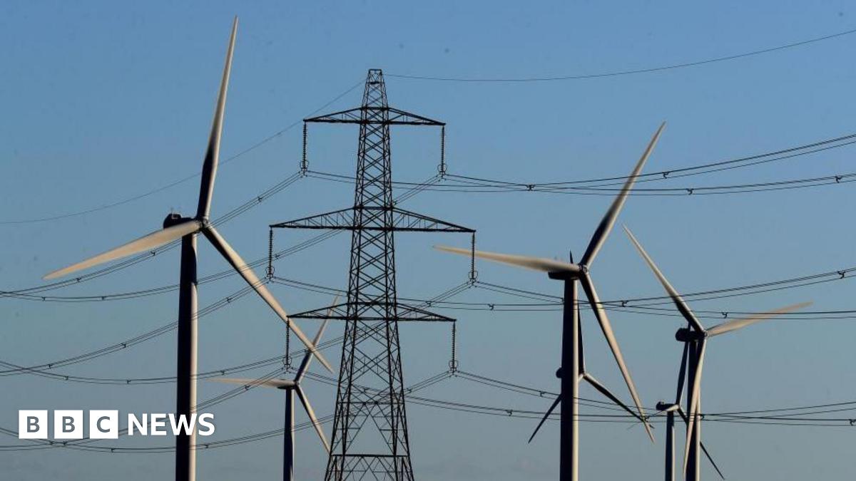 Six wind turbines in front of electricity pylons, with a light blue sky in the background.