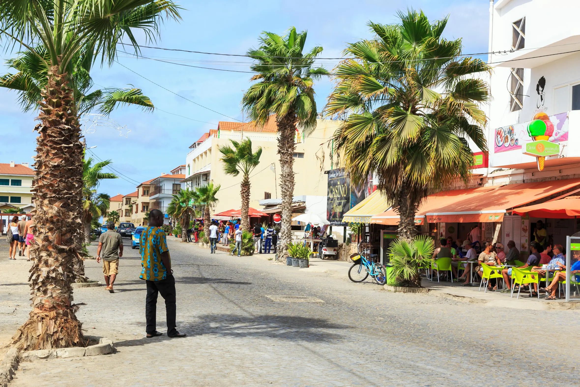 Main street in Santa Maria, Sal, Cape Verde, with shops, souvenir stalls, and restaurants under palm trees.