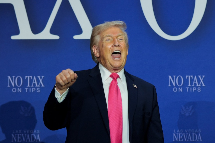 Trump holds one hand in a fist as he gestures while speaking on a stage.