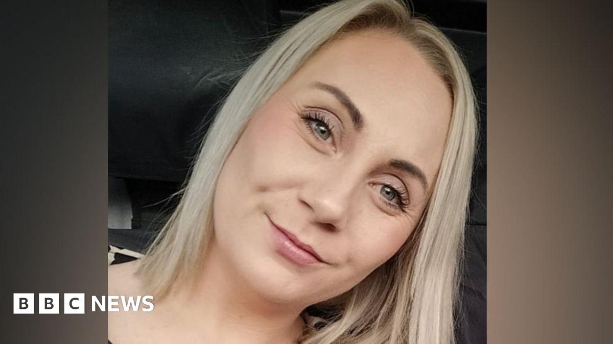 Allison Rowe who has short greying hair with pursed lips and wearing maroon rimmed round glasses and a denim top