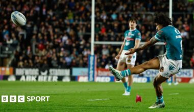 St Helens full-back Tristan Sailor (right, in green shirt and white shorts) kicks for goal against Catalans Dragons with a team-mate watching in the background.
