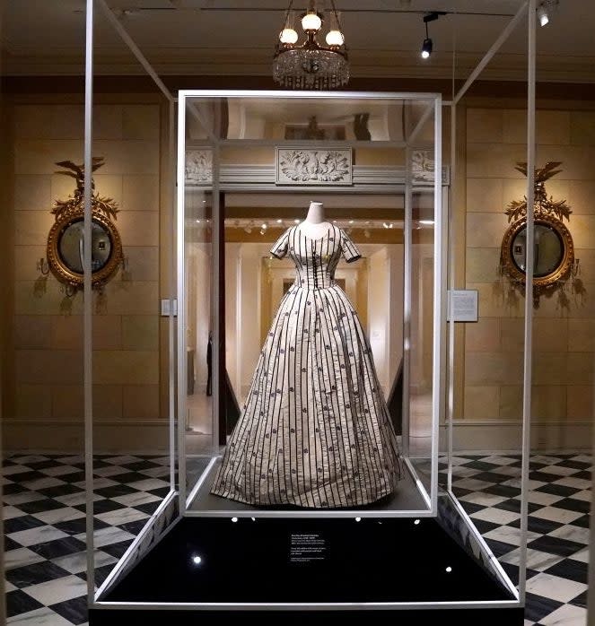 A historical gown displayed in a glass case within an elegant museum setting