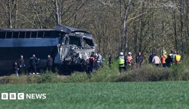 A train is on the left of the image with the front section seriously damaged. Emergency services in hi-vis are on the scene
