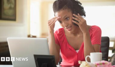 A woman stares at her computer screen while talking on the phone. She looks frustrated