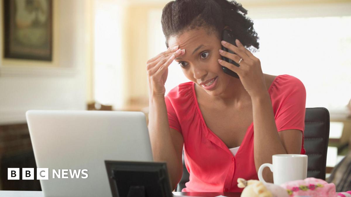 A woman stares at her computer screen while talking on the phone. She looks frustrated