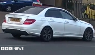 A CCTV still of a white Mercedes being driven along a road.
