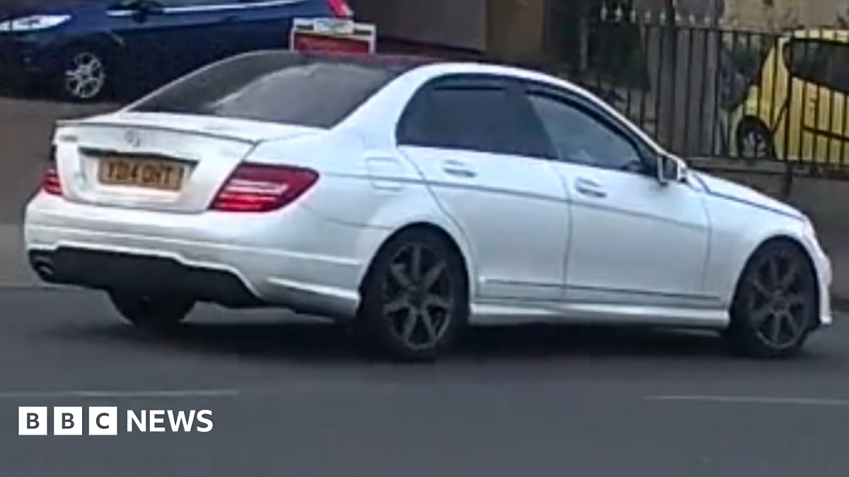 A CCTV still of a white Mercedes being driven along a road.
