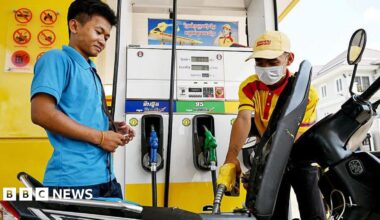 An employee pumps fuel into a motorbike as a customer his right watches