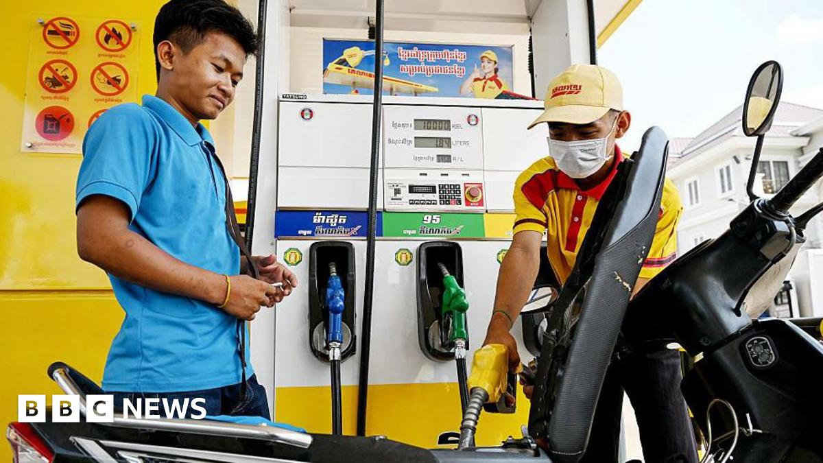 An employee pumps fuel into a motorbike as a customer his right watches