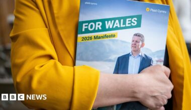 A woman in a yellow jacket holding a copy of the Plaid Cymru manifesto, which reads "for Wales" in capital letters and "2026 manifesto". The cover of the manifesto shows Rhun ap Iorwerth looking off into the distance.