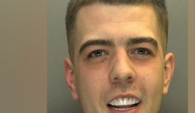 A custody photo of Coran Davies. Davies smiles looking at the camera. His white teeth are on show.