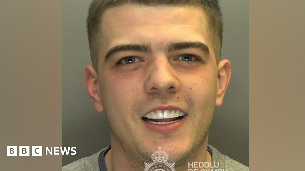 A custody photo of Coran Davies. Davies smiles looking at the camera. His white teeth are on show.