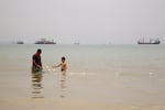 A boy walks near a man with a fishing net as ships are anchored near the shoreline in Bandar Abbas, an Iranian port city and the capital of Hormozgan province, along the Persian Gulf and Strait of Hormuz.