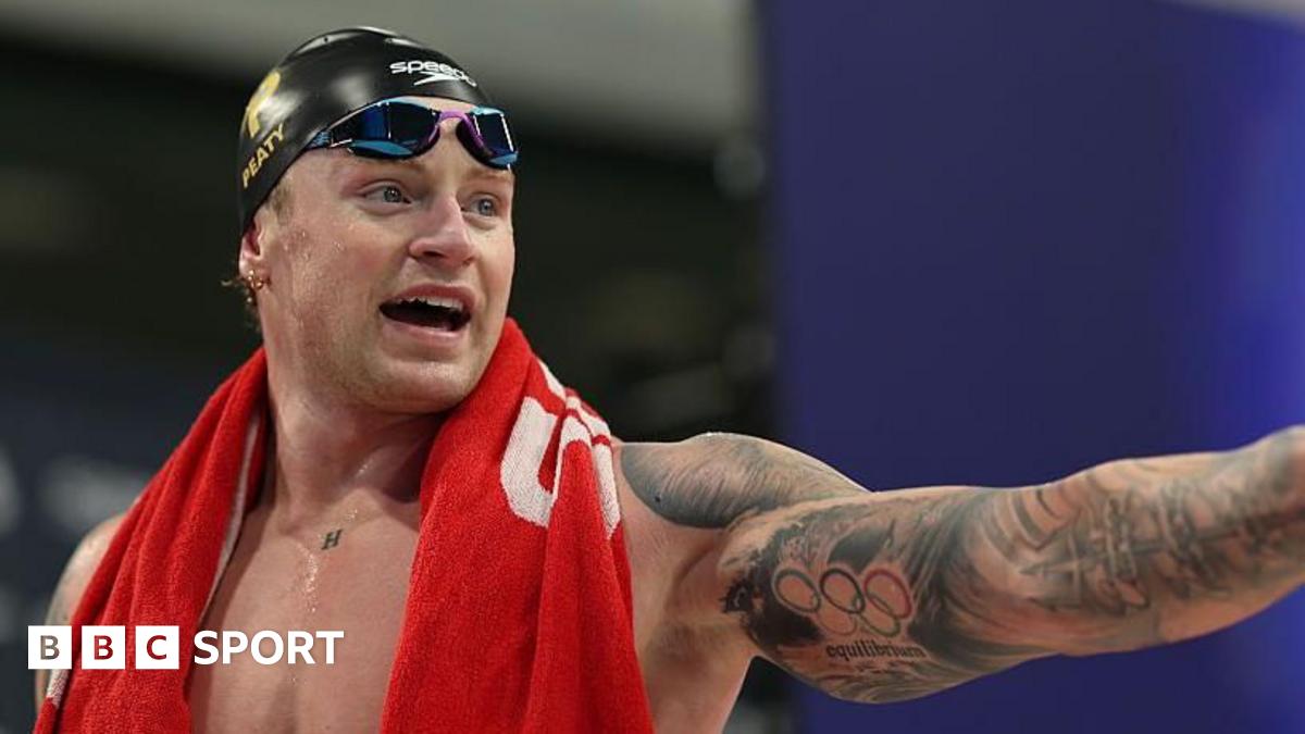 Adam Peaty in the swimming pool with a red swimming cap on. He is leaning on a floating lane divider