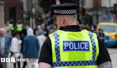 The back of the head of a policeman in uniform on patrol in a city, blurred out people are seen in front of him