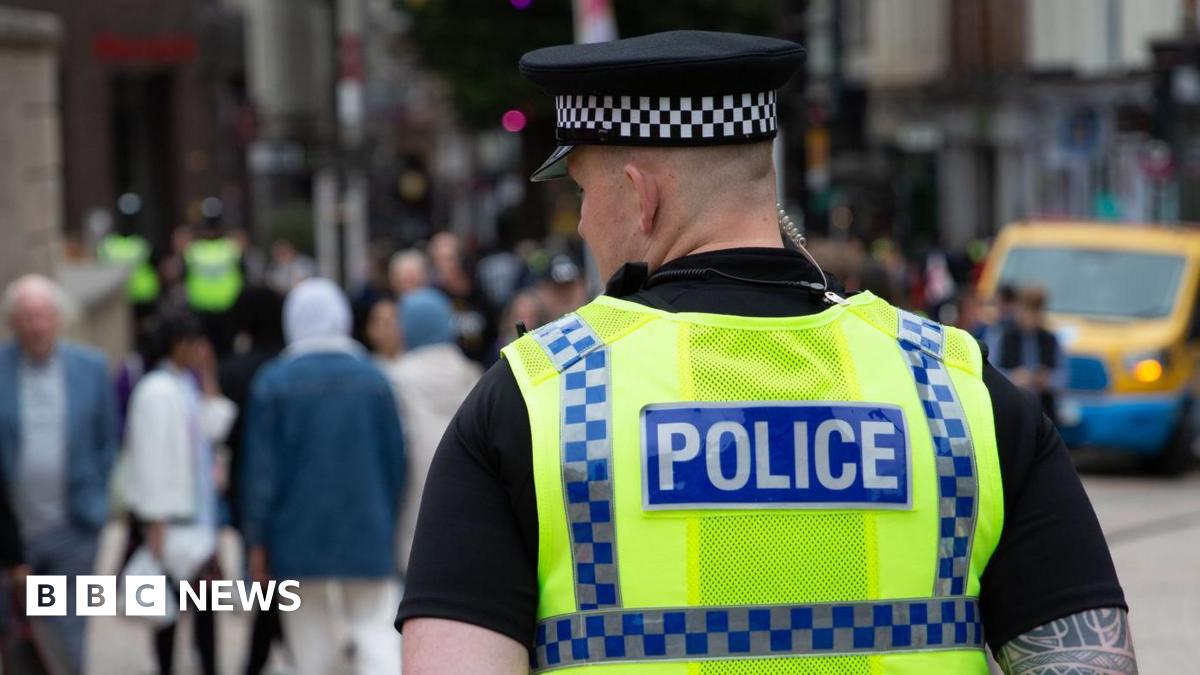 The back of the head of a policeman in uniform on patrol in a city, blurred out people are seen in front of him