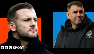 Jack Wilshere, wearing a black coat with a high collar, looks on with a serious face (left). Dave Challinor, wearing a black jacket with a Stockport county badge on, smiles (right).