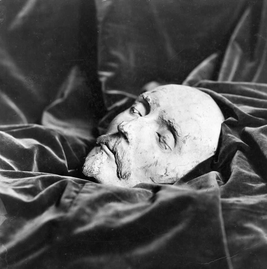 A sculpted mask of a man's face with a mustache lies on a cloth backdrop