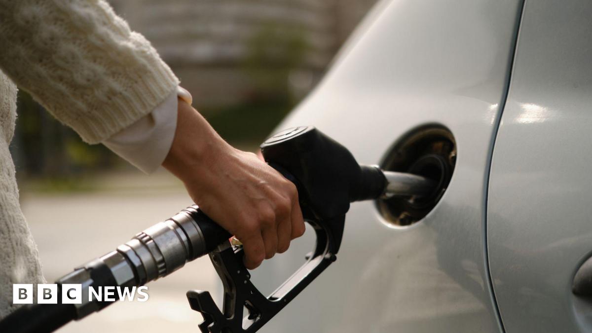 A woman using a gas pump to refuel vehicle during energy crisis. She has a silver car, and is wearing a white sweater.