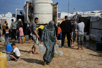 Samah Abu Daqqa, 33, carries jerrycans filled with water through a tent camp in Khan Younis, in the southern Gaza Strip, Thursday.