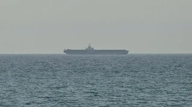 A large tanker ship seen on the horizon on the sea. It's a grey day with a hazy sky and rippled sea