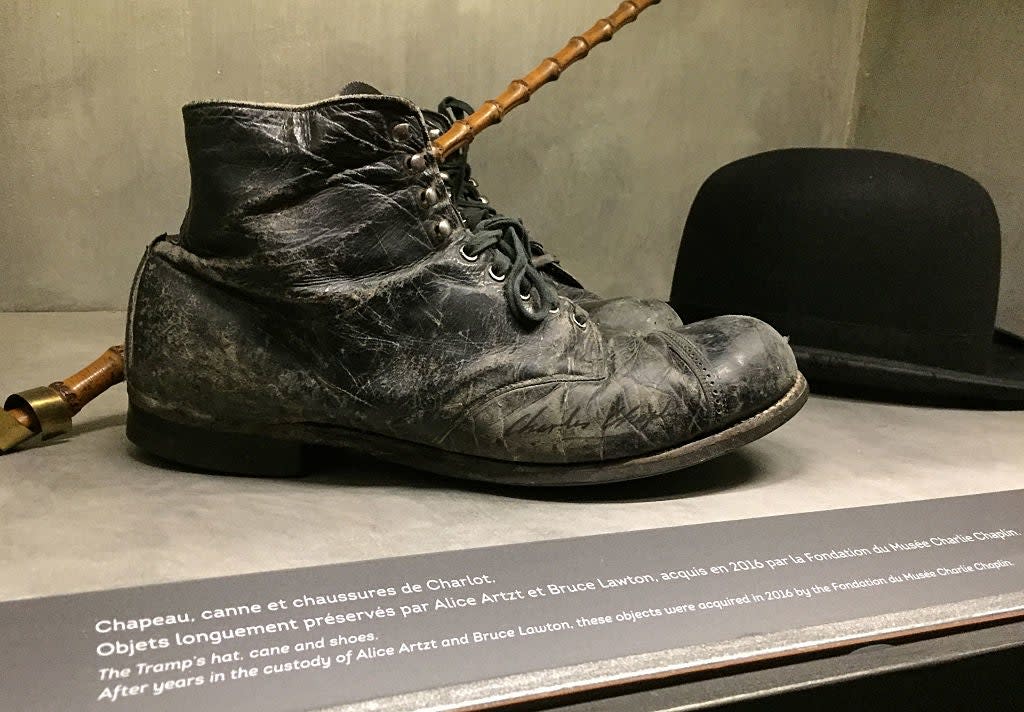 Charlie Chaplin's iconic cane, bowler hat, and worn-out boots on display with informational plaque in a museum setting