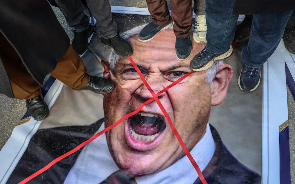 Protestors stand on an image of Benjamin Netanyahu during a demonstration to protest against the US-Israel war on Iran