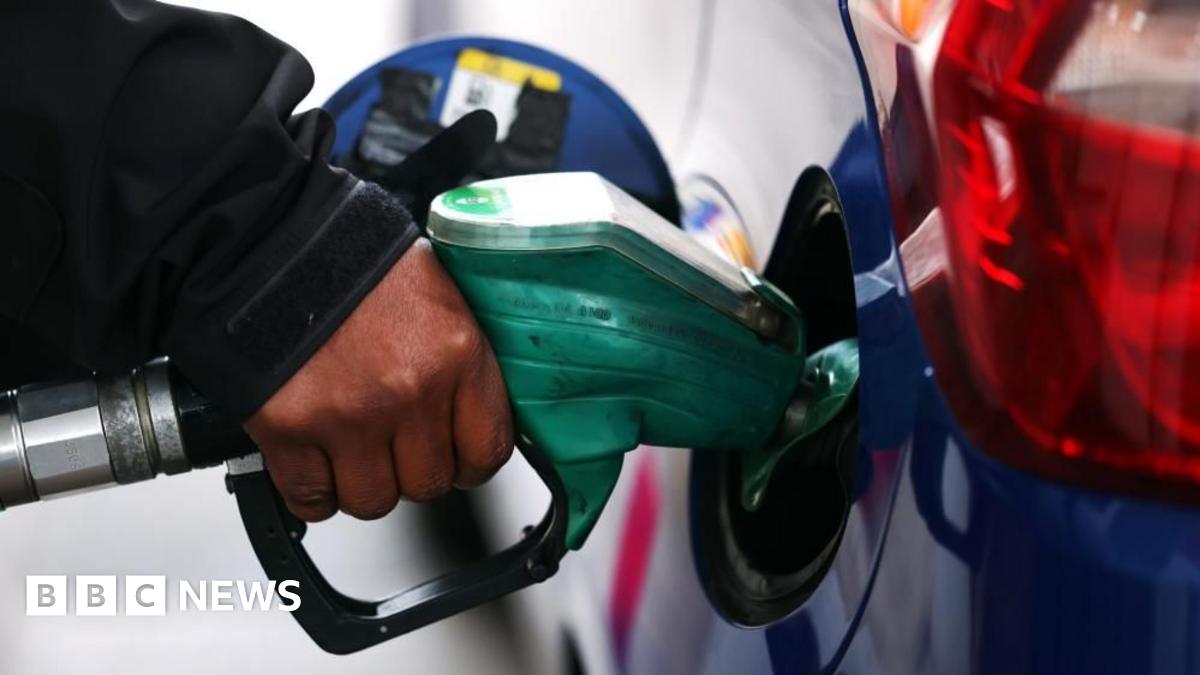 A close up of someone's hand on the pump while they fill their blue car with petrol