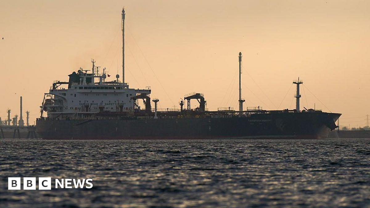 An oil tanker at sea silhouetted against a sky at sunset.