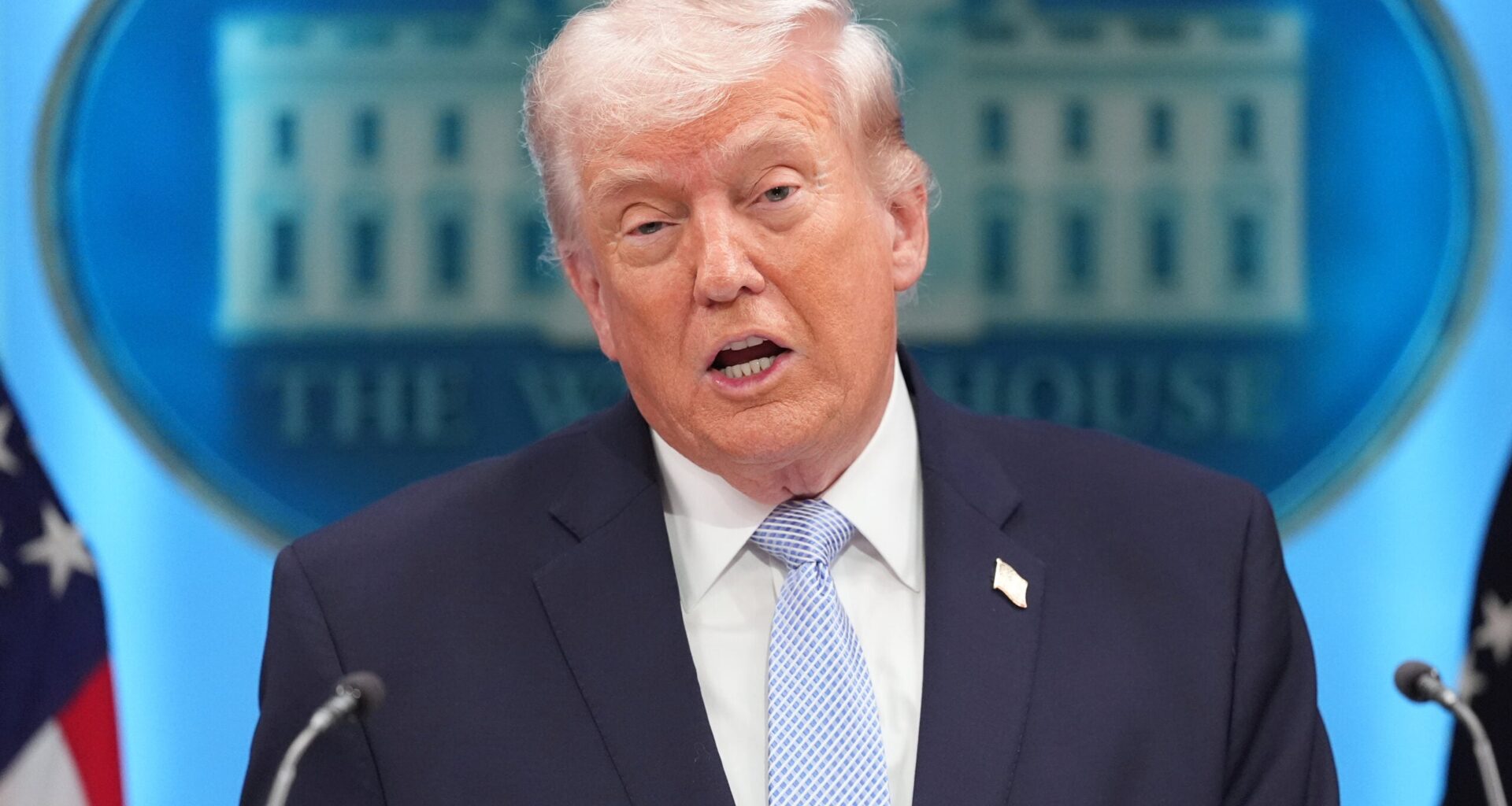 A man in a suit and tie speaks at a podium, with the White House emblem visible in the background.