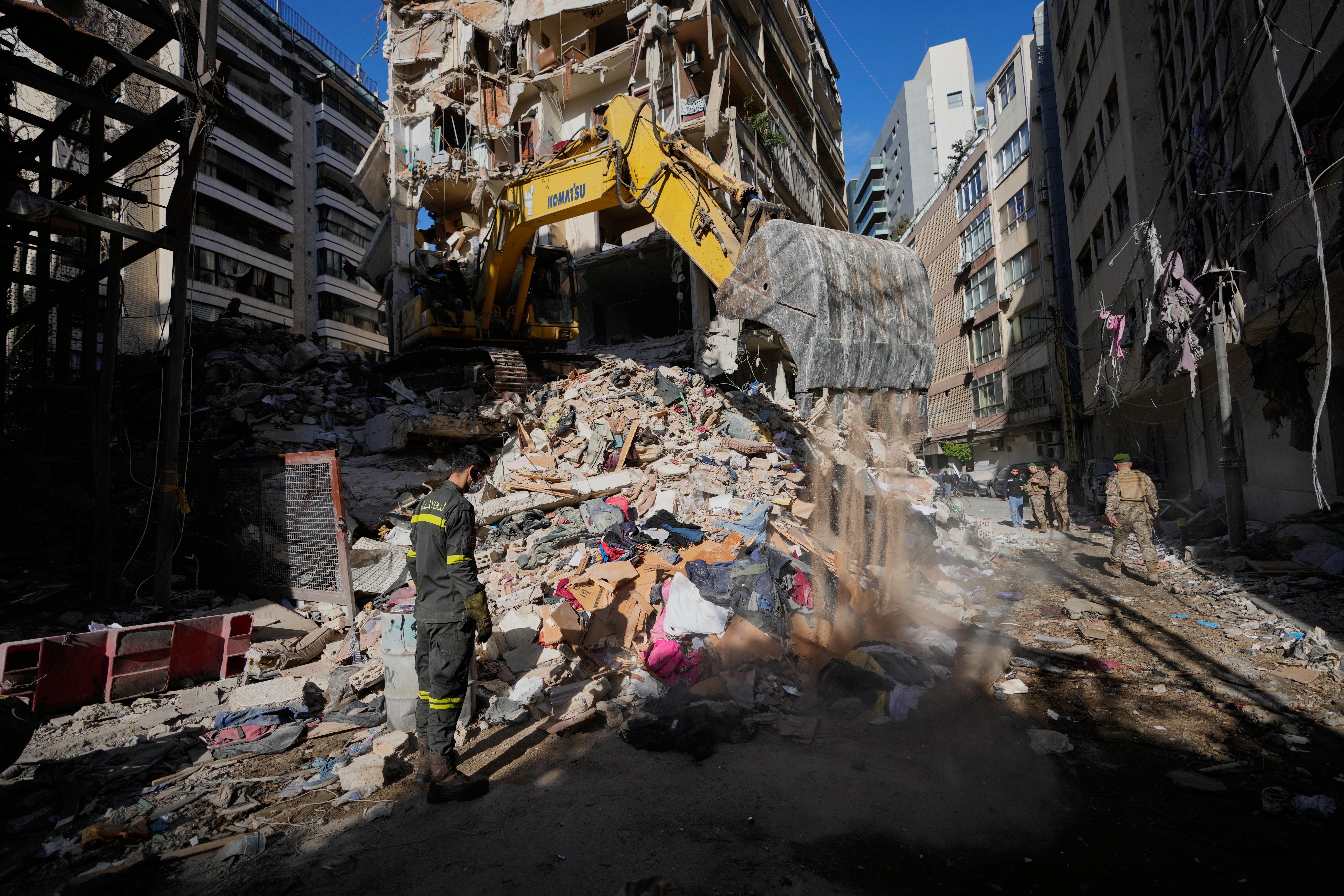 A Lebanese civil defense worker looks on as an excavator operates on a destroyed building.