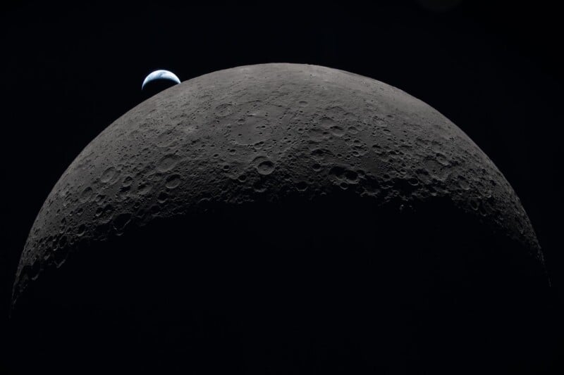 A view of the Moon’s cratered surface dominates the foreground, with the distant Earth partially visible, rising over the Moon’s horizon against the darkness of space.