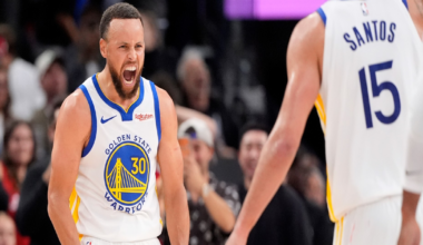 Stephen Curry, wearing a Golden State Warriors jersey, clenches his fists and yells while teammate Santos, number 15, approaches him.