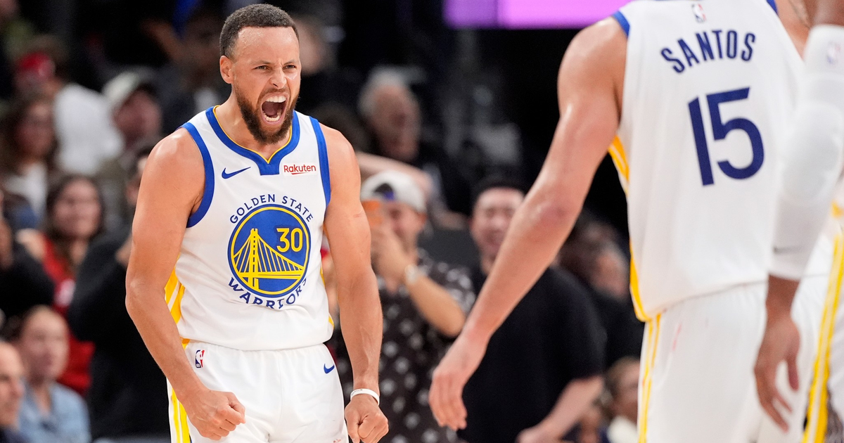 Stephen Curry, wearing a Golden State Warriors jersey, clenches his fists and yells while teammate Santos, number 15, approaches him.