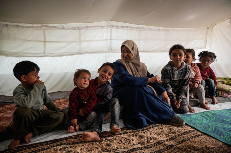 Inaam sits with her six grandchildren, the children of one of her sons who has been held in Israeli prisons for two years [Omar Ashtawy/ Al Jazeera]