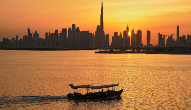 The Dubai skyline seen at sunset over the water, with a boat traveling by.