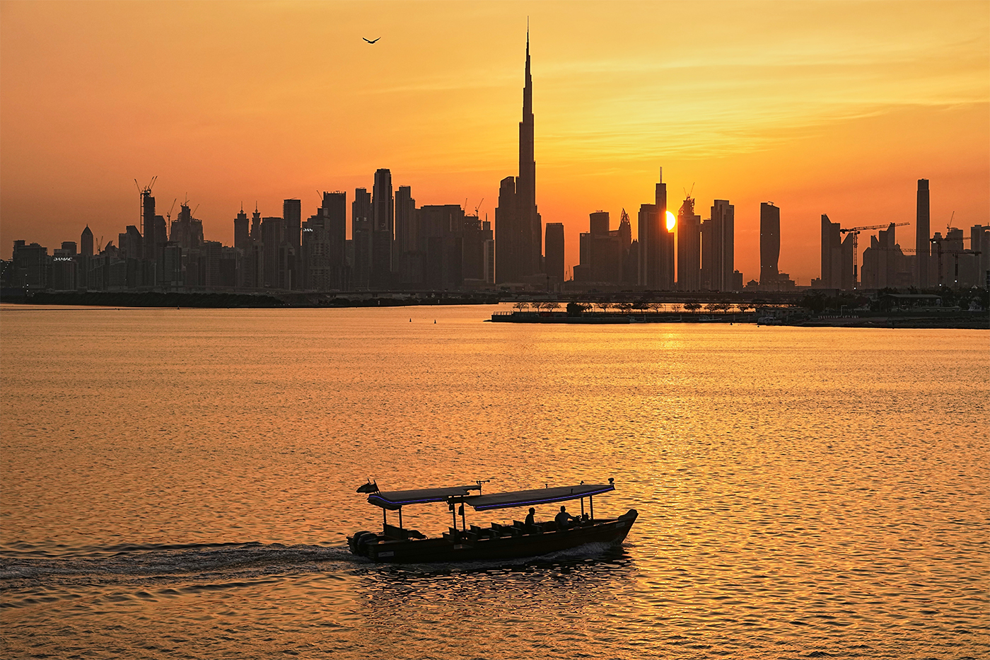 The Dubai skyline seen at sunset over the water, with a boat traveling by.