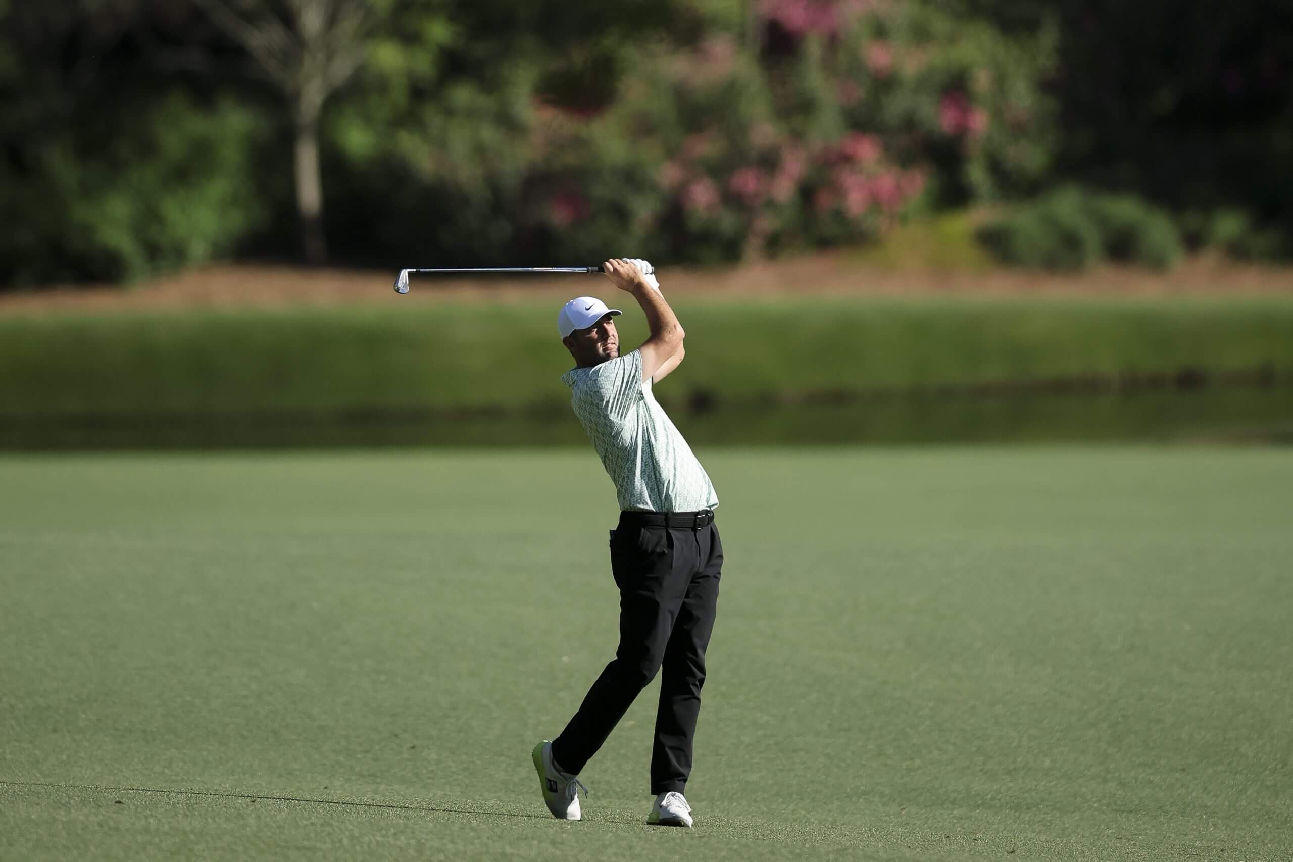 Scottie Scheffler, positioned in his follow-through, watches his ball after hitting it on the fairway.