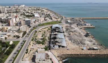 Backdropped by ships in the Strait of Hormuz, damage, according to local witnesses caused by several recent airstrikes during the U.S.-Israel military campaign, is seen on a fishing pier in the port of Qeshm island, Iran, Monday, April 13, 2026. (AP Photo/Asghar Besharati)