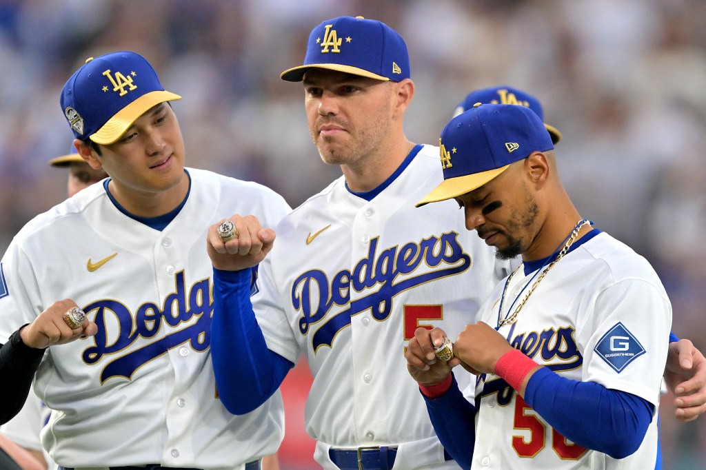 Three baseball players in blue and white Dodgers uniforms with gold-brimmed hats showing off large rings on their hands.