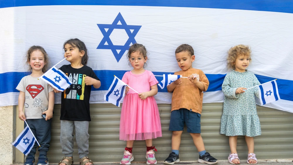 A group of children standing in front of a large Israeli flag.