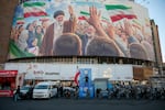 A police officer stands holding a flag in Valiasr Square beneath a mural of the late Ayatollah Ali Khamenei in Tehran, Iran, on Thursday.