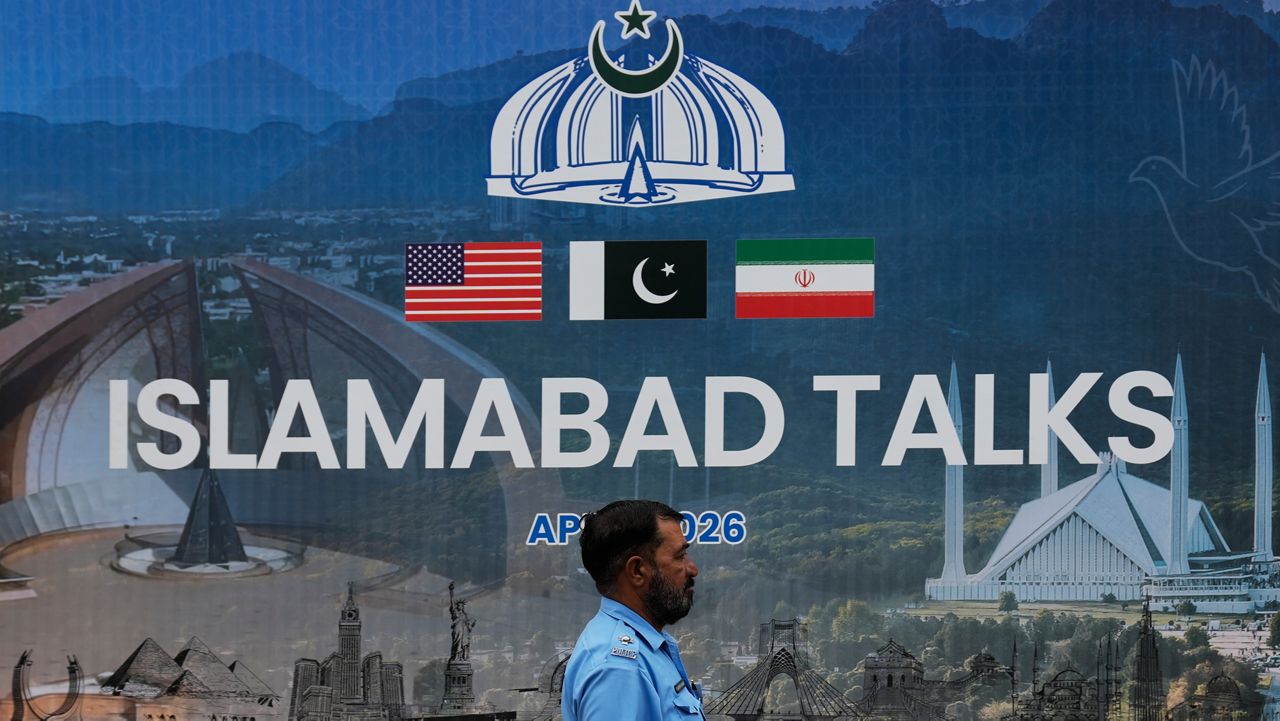 A police officer walks past a billboard regarding the United States and Iran negotiations, outside a media facilitation center in Islamabad, Pakistan, Saturday, April 11, 2026. (AP Photo/Anjum Naveed)