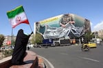 A woman holds Iran's national flag while standing near a billboard with a sentence reading "The Strait of Hormuz remains closed" at the Enqelab Square in Tehran, on April 5, 2026.