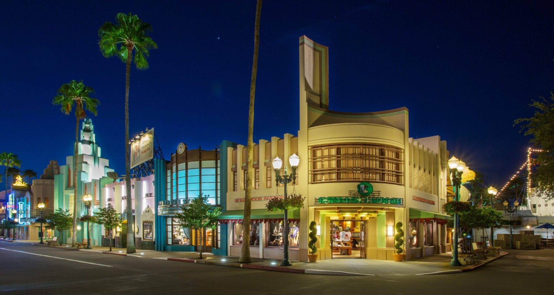 A street scene at night with art deco buildings, illuminated storefronts, and palm trees under a clear sky evokes the vibrant charm of Walt Disney World. Amid the glow, a purple Mickey molded Loungefly bag adds a touch of whimsy to the enchanting atmosphere.