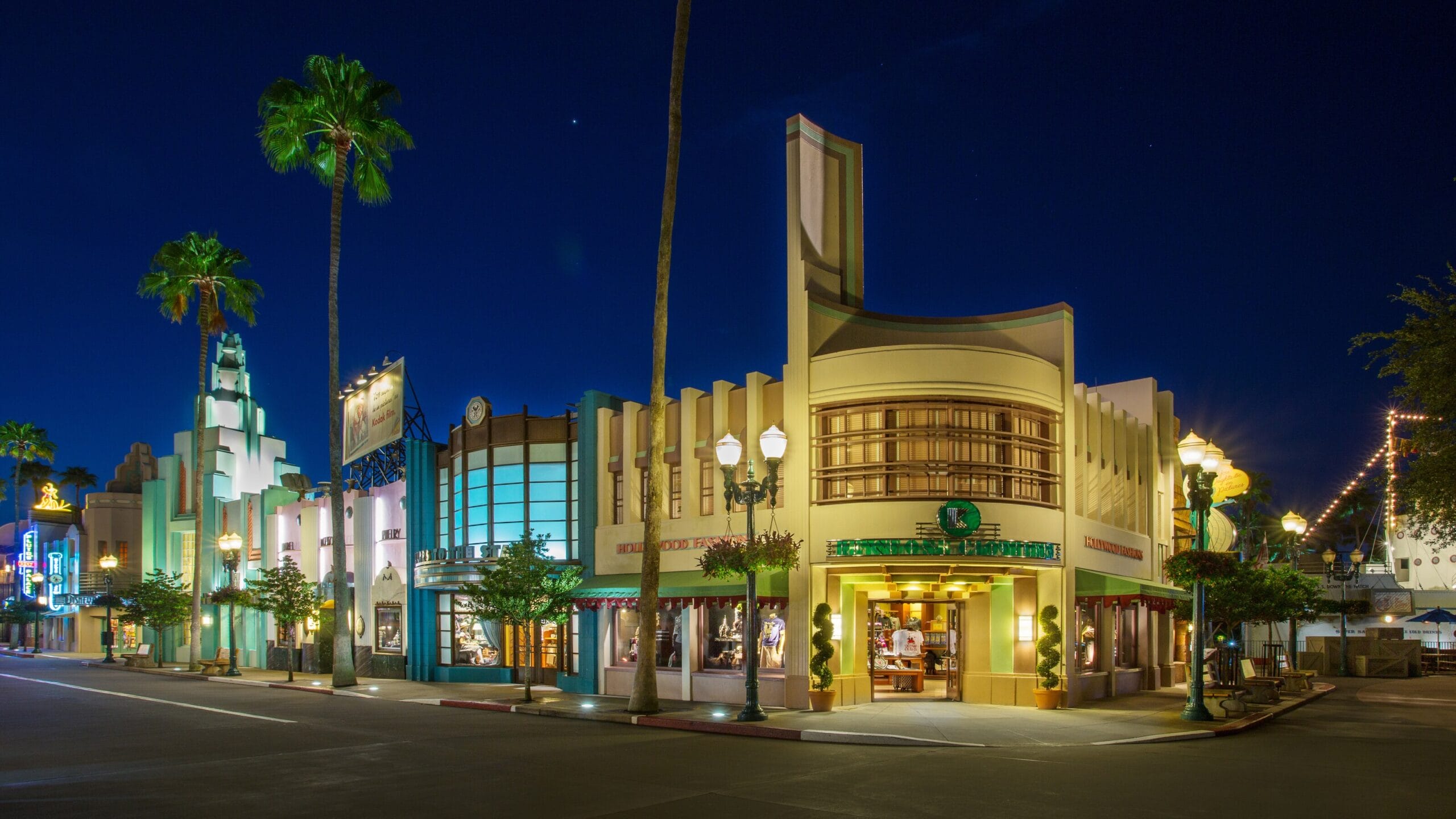 A street scene at night with art deco buildings, illuminated storefronts, and palm trees under a clear sky evokes the vibrant charm of Walt Disney World. Amid the glow, a purple Mickey molded Loungefly bag adds a touch of whimsy to the enchanting atmosphere.