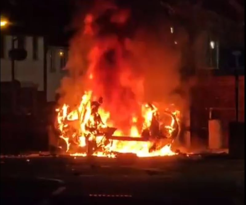 A still from a video posted on social media showing a car on fire outside Dunmurry PSNI station.
