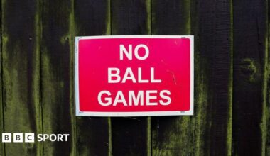 A red 'no ball games' sign on a fence