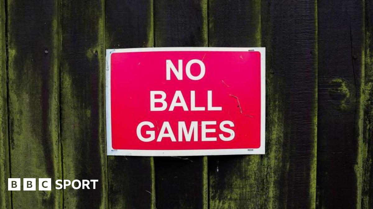 A red 'no ball games' sign on a fence