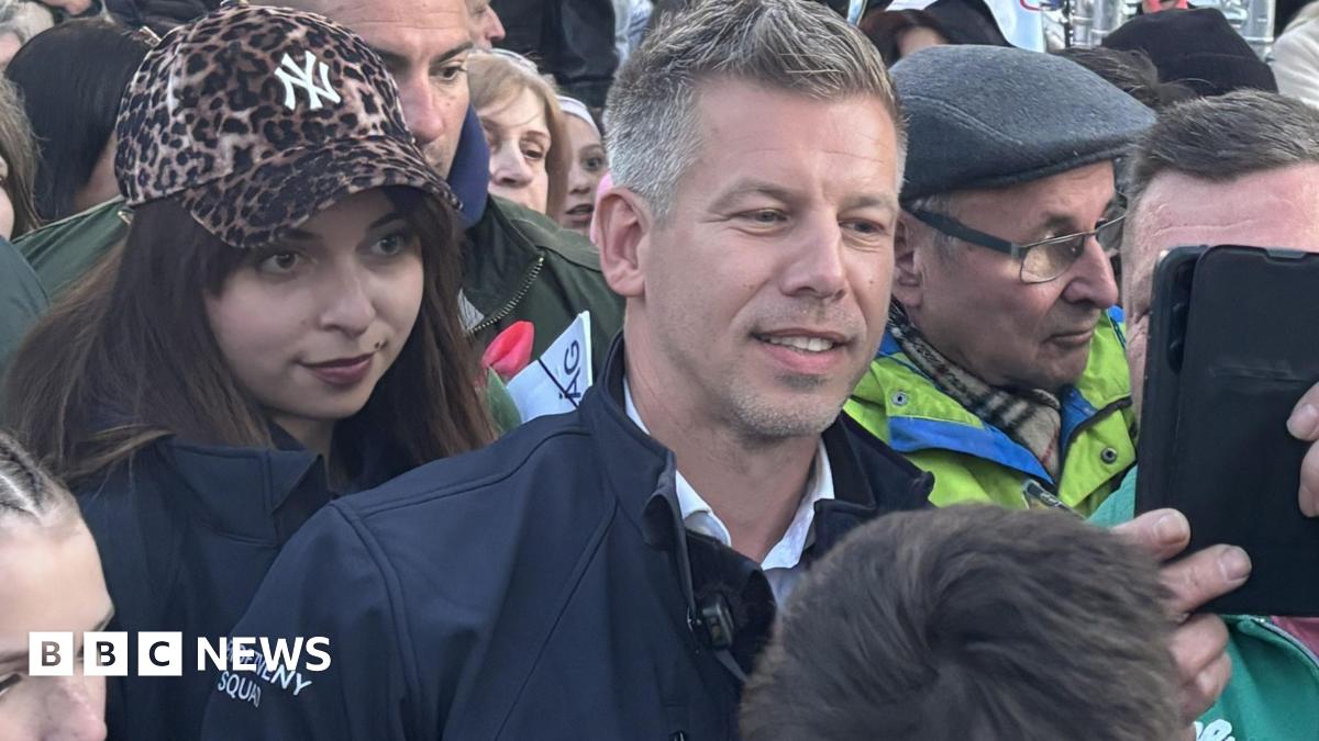 A man in green takes a selfie with a man with short hair and a blue jacket